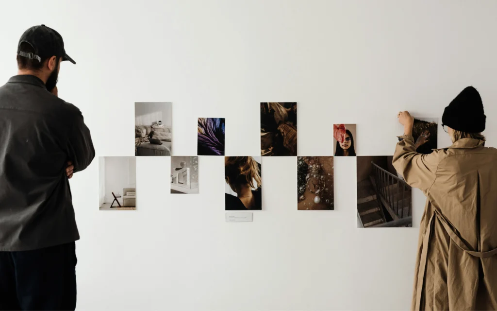 Two designers pinning visual mood board photos to a wall, curating brand concepts and AI creative workflow assets.