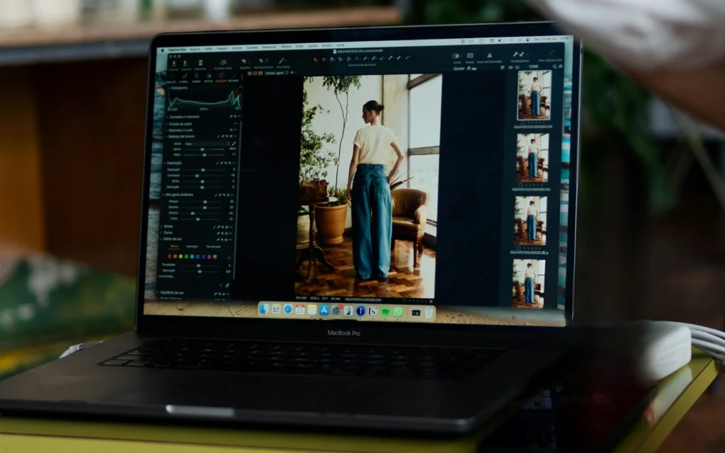 MacBook Pro displaying photoshoot color editing software Capture One with a fashion portrait of a model in wide-leg jeans on screen and a shot list gallery in the sidebar.