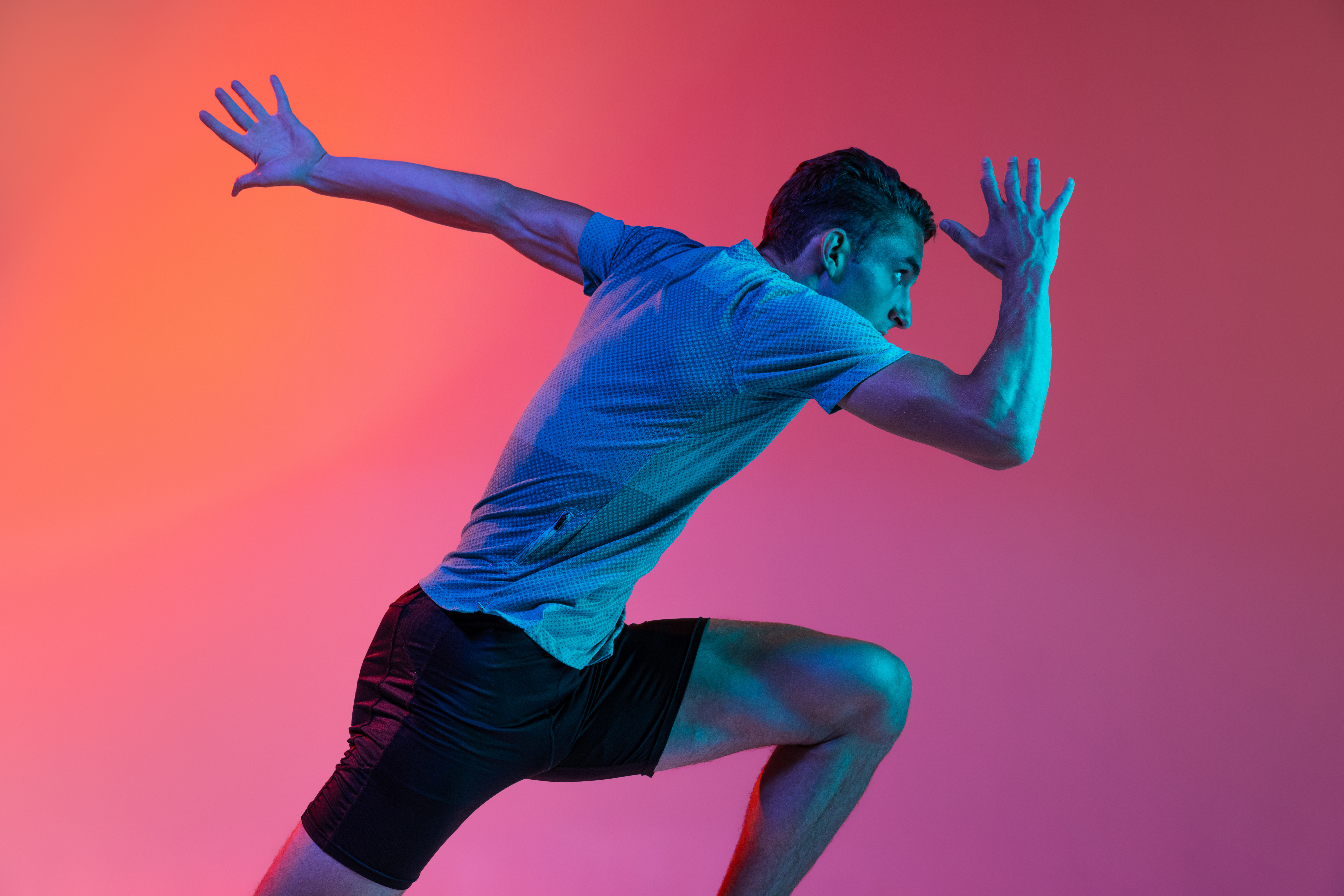 Side view. Portrat of Caucasian male athlete, runner training isolated on pink studio background with blue neon filter, light. Concept of action, motion, speed, healthy lifestyle. Copyspace for ad.
